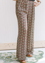 Model wearing black wide leg polyester pants with a gold, rose and green pattern and pockets. 