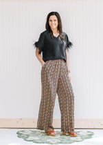 Model wearing a black top with wide leg pants with a gold, rose and green pattern and pockets. 