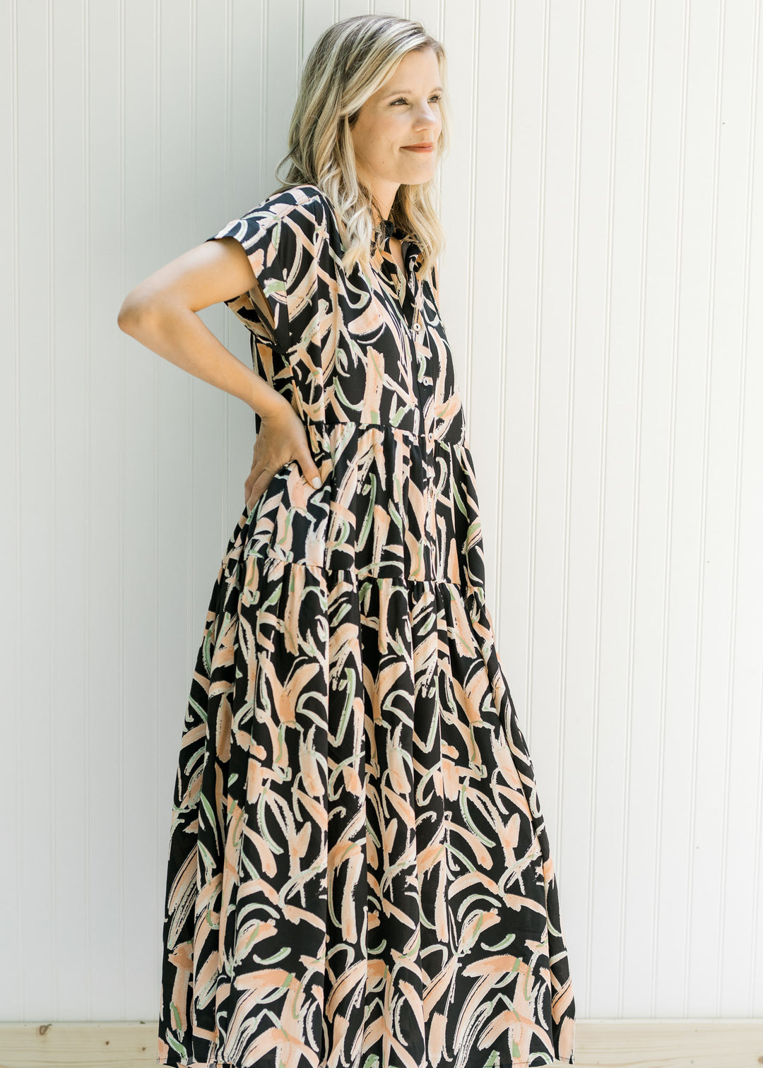 Model wearing sandals with a black button up midi polyester dress with tiers and short sleeves.