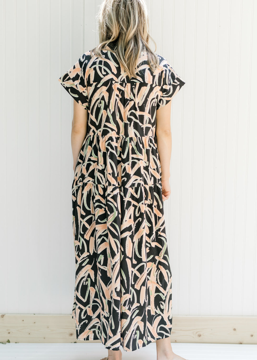Back view of Model wearing a black button up midi dress with tiers and short sleeves.