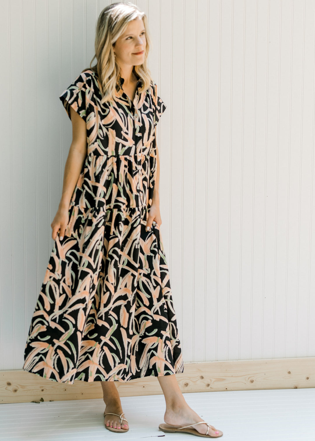 Model wearing sandals with a black button up midi dress with tiers and short sleeves.