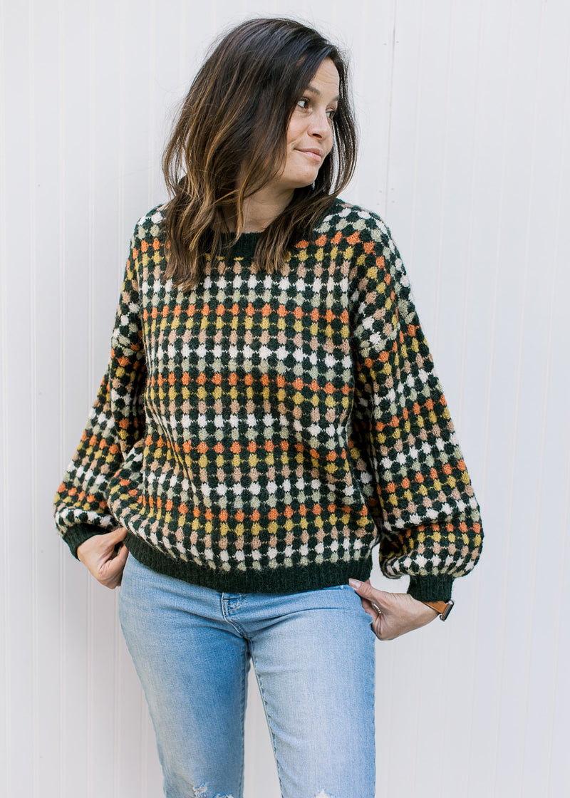 Model wearing jeans with a navy sweater with fall colored dots, long sleeves and a round neck.