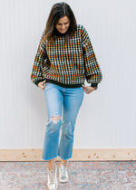 Model wearing jeans, sneakers and a navy sweater with fall colored dots and bubble long sleeves. 