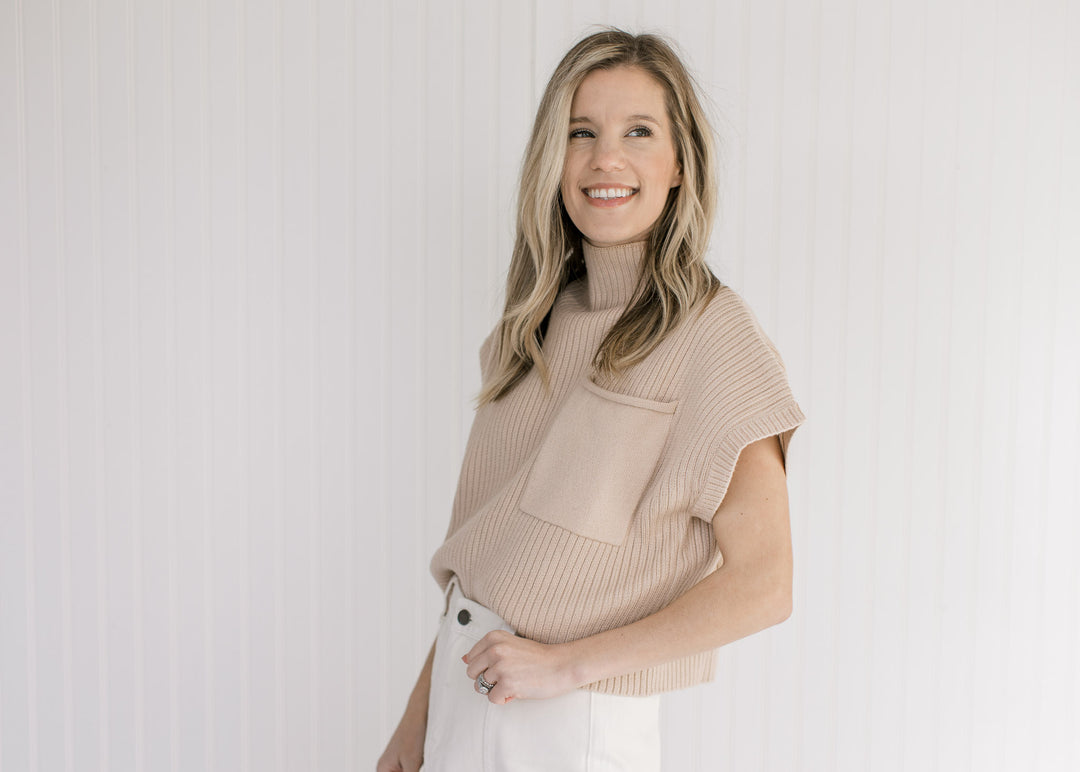 Model wearing white skirt with a tan cable knit sweater vest with a patch pocket.