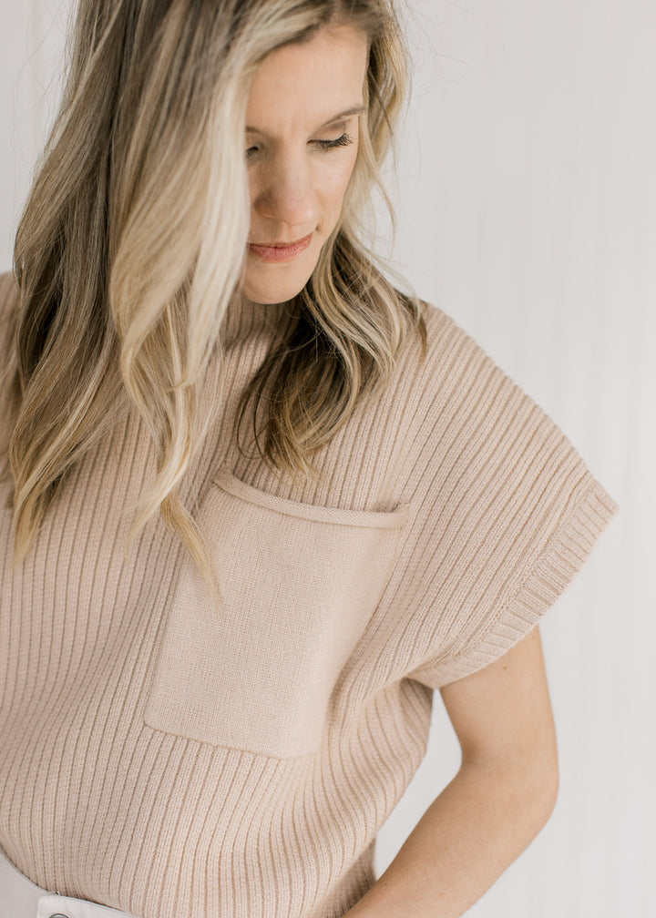 Close up of patch pocket on a tan cable knit sweater vest with a mock neckline. 