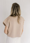 Back view of Model wearing a tan cable knit sweater vest with a patch pocket and a mock neckline.