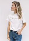 Model wearing a white short sleeve tee with the word bonjour embroidered across the bust in tan. 