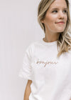 Model wearing a white short sleeve tee in cotton with bonjour embroidered across the bust in tan. 