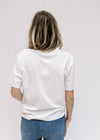 Back view of Model wearing a white short sleeve tee composed of cotton with a round neckline. 