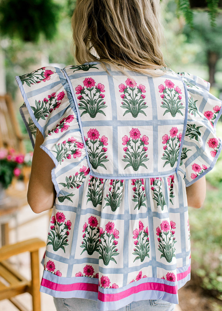 Back view of Model wearing an off white top with pale blue squares and pink flowers.