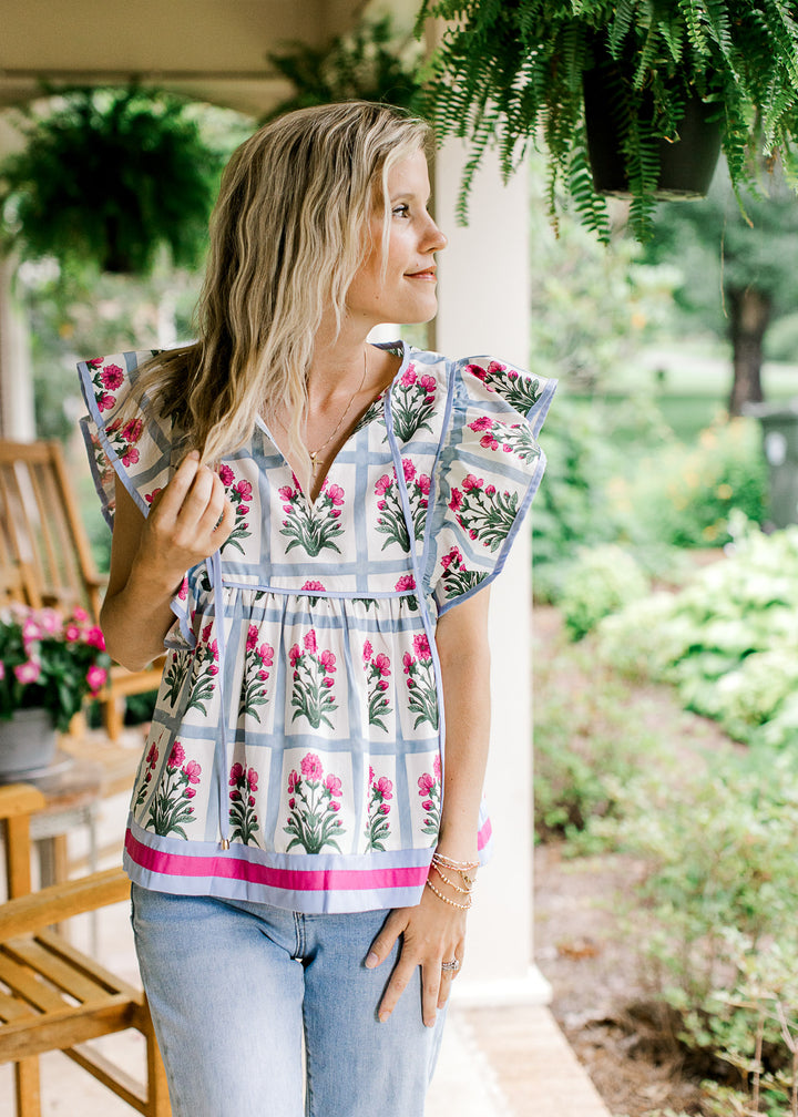 Model wearing jeans and an off white top with blue squares and pink flowers and ruffle cap sleeves.