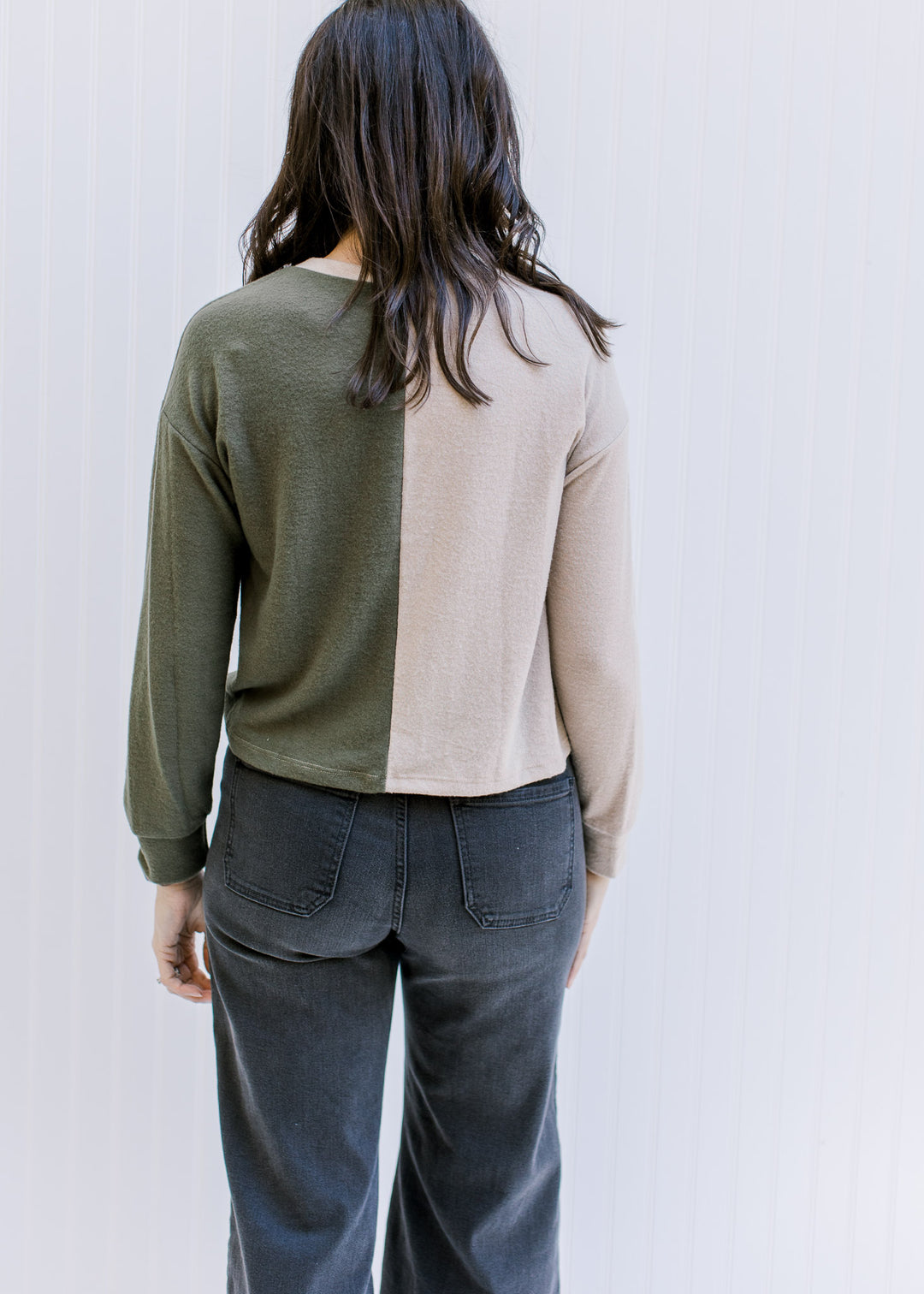 Back view of a model wearing a camel and forest green color block sweater with long sleeves. 