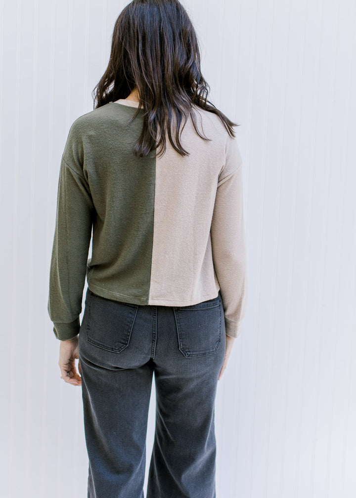 Back view of a model wearing a camel and forest green color block sweater with long sleeves. 