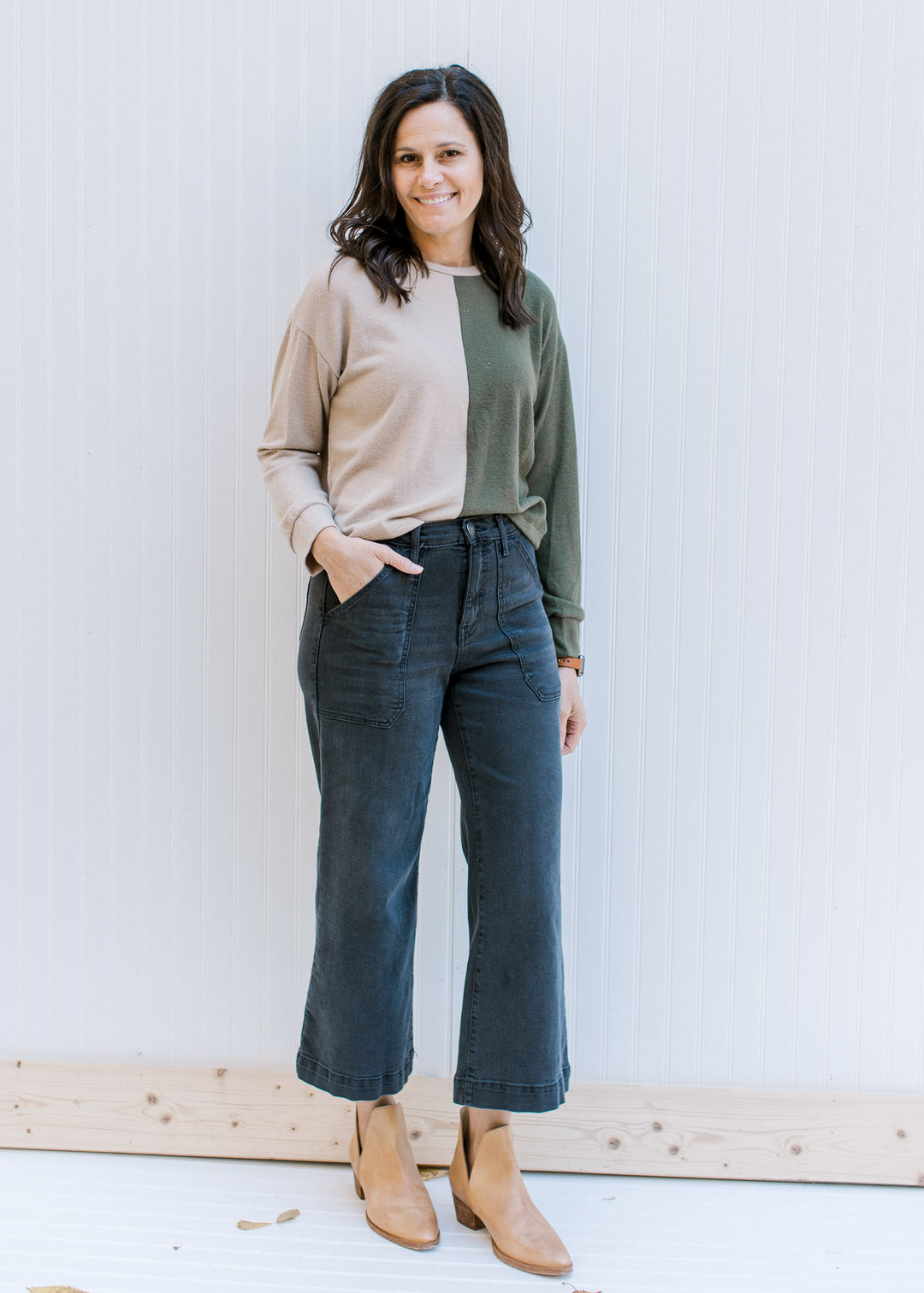 Model wearing jeans with a camel and forest green color block sweater with long sleeves. 
