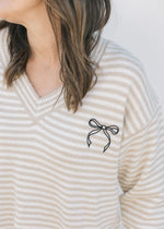 Close up of black bow graphic on a cream and tan striped v-neck sweater with long sleeves. 