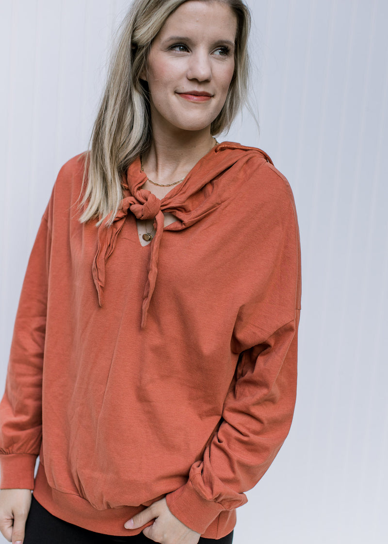 Model wearing a brick long sleeve sweatshirt with an extended shoulder, hood and v-neck with a tie. 
