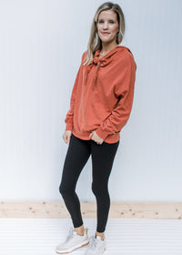 Model wearing jeans with a brick long sleeve sweatshirt with a hood and v-neck with a tie. 