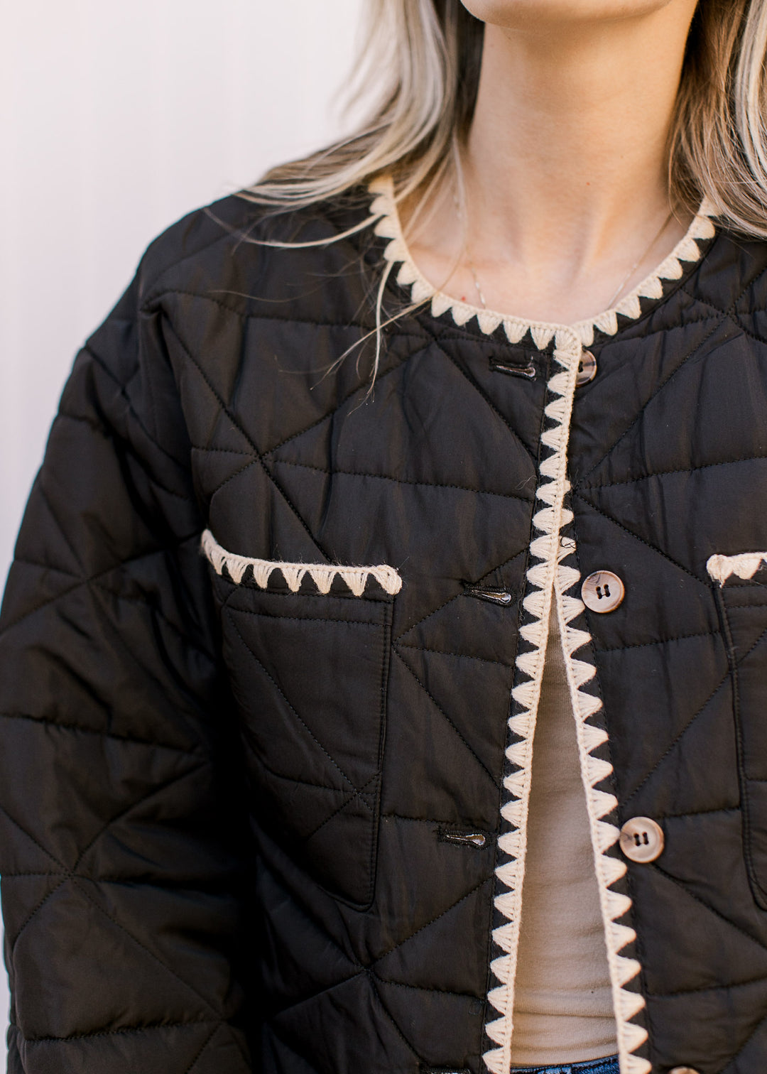 Model wearing a black puffer jacket with cream stitching, button front and two front pockets.