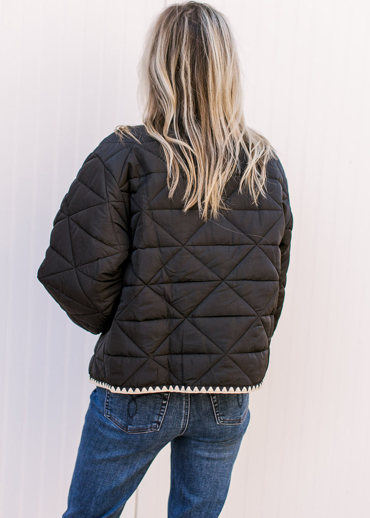 Back view of Model wearing a black jacket with cream stitching, button front and long sleeves. 