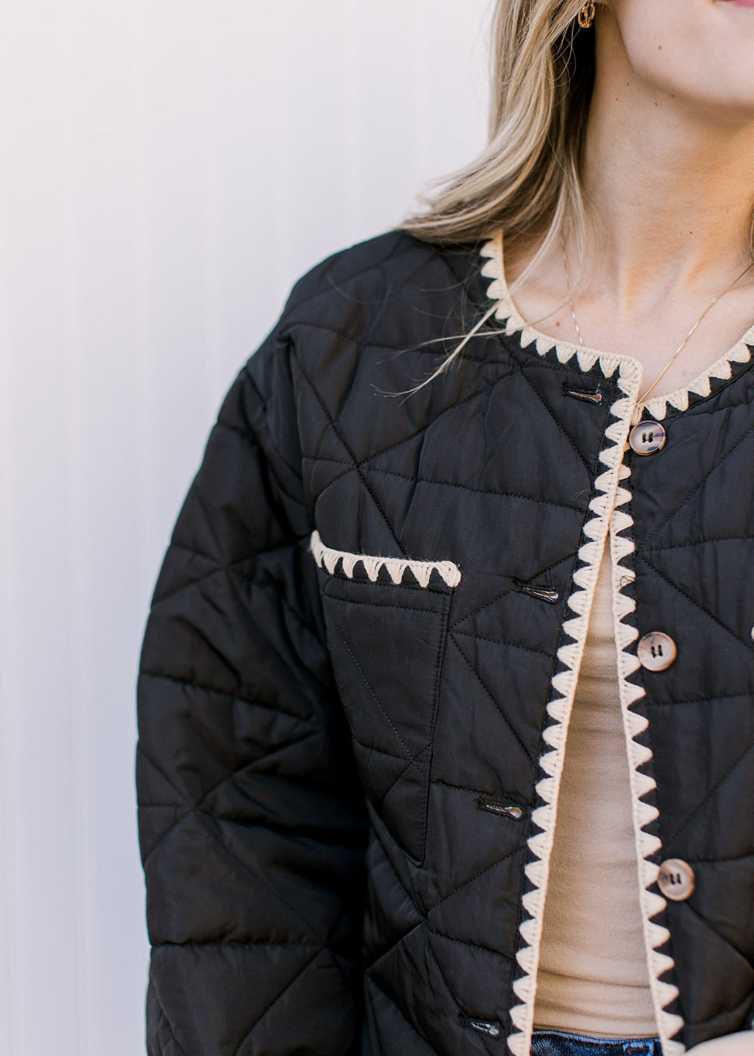 close up of cream stitching detail on a black jacket with two front patch pockets and long sleeves. 