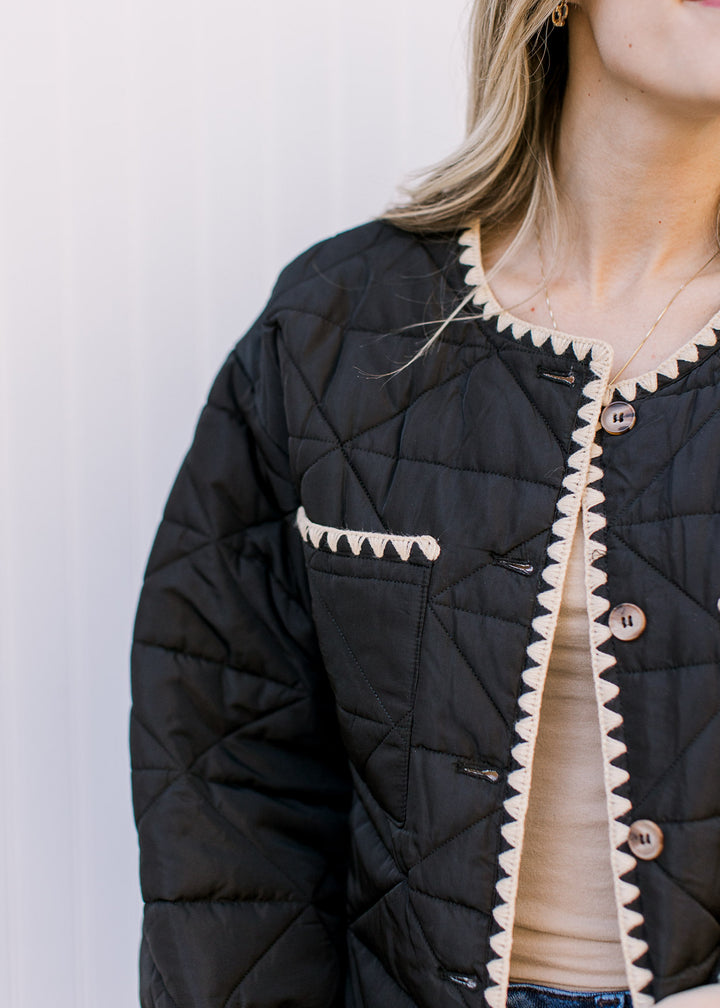 close up of cream stitching detail on a black jacket with two front patch pockets and long sleeves. 