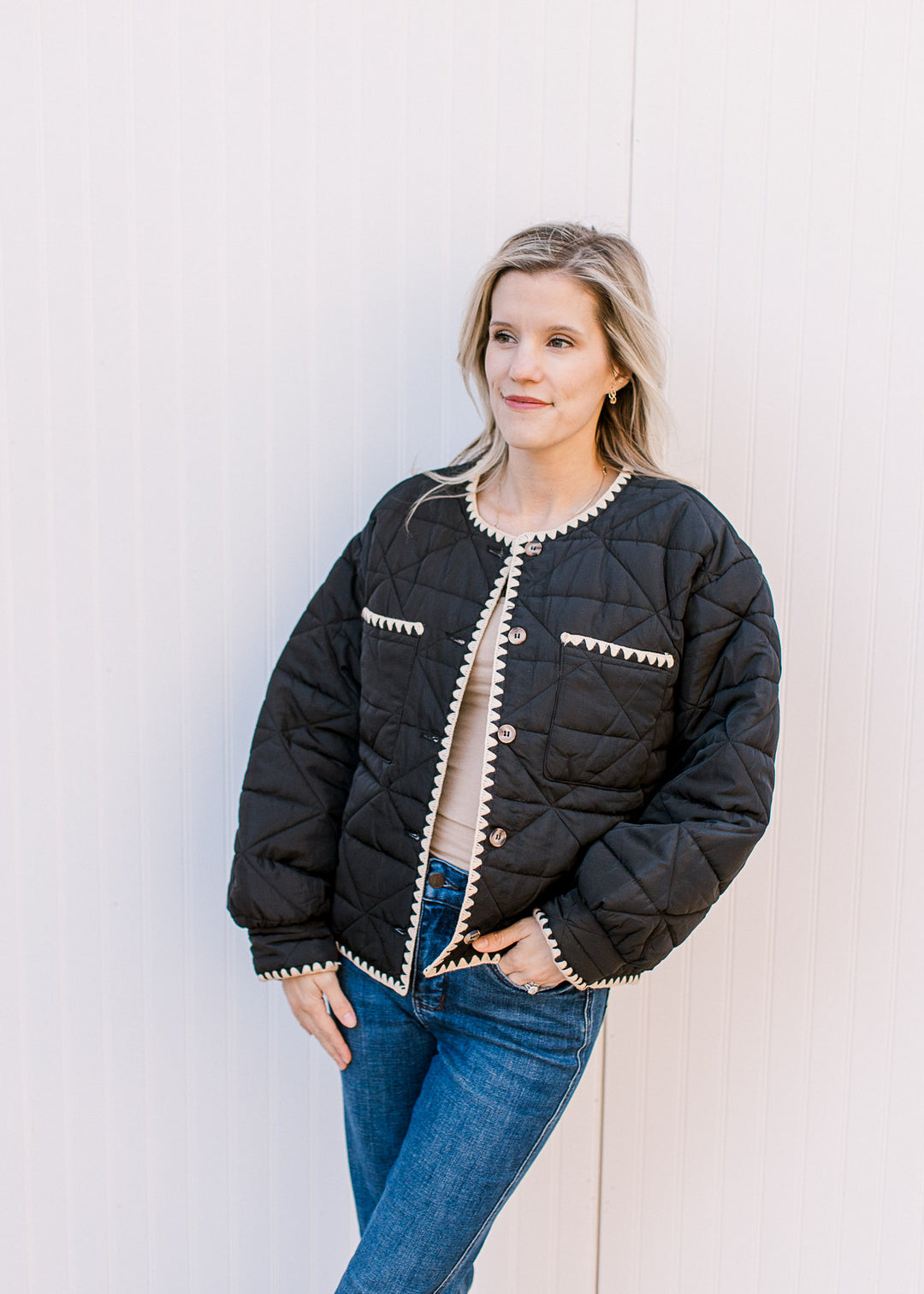 Model wearing jeans and a black jacket with cream stitching details, button front and front pockets.