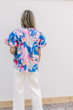 Back view of Model wearing bright floral top with a smocked yolk, keyhole and short puff sleeves.