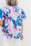 Close up of the back on a bright floral top with a smocked yolk, ruffle neck and short puff sleeves.