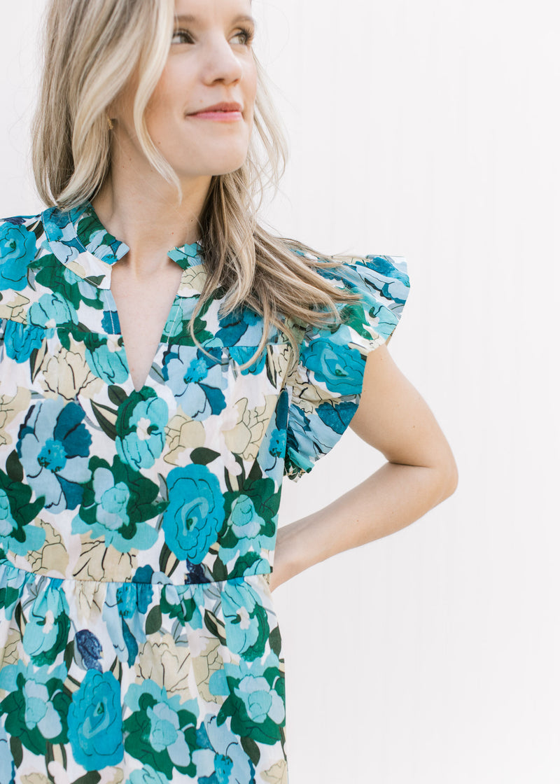 Close up of v-neck and ruffle cap sleeve on a bright blue floral dress, hitting just above the knee.