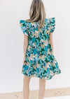 Back view of Model wearing a tiered bright blue floral dress with ruffle cap sleeves and a v-neck.
