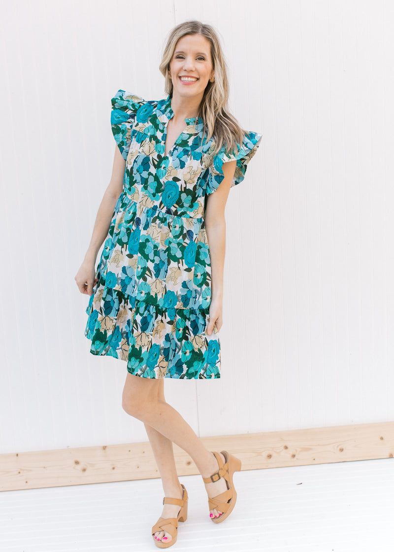 Model wearing an above the knee bright blue floral dress with ruffle cap sleeves and a v-neck.