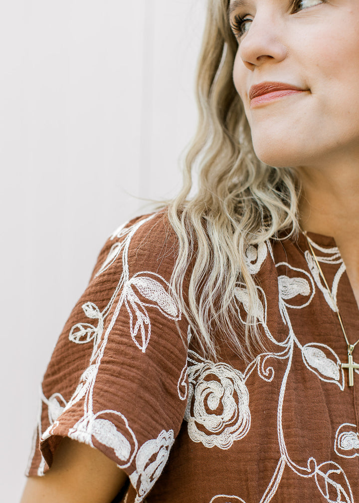 Close up of short sleeve and v-neck on a brown midi with cream embroidered flowers. 