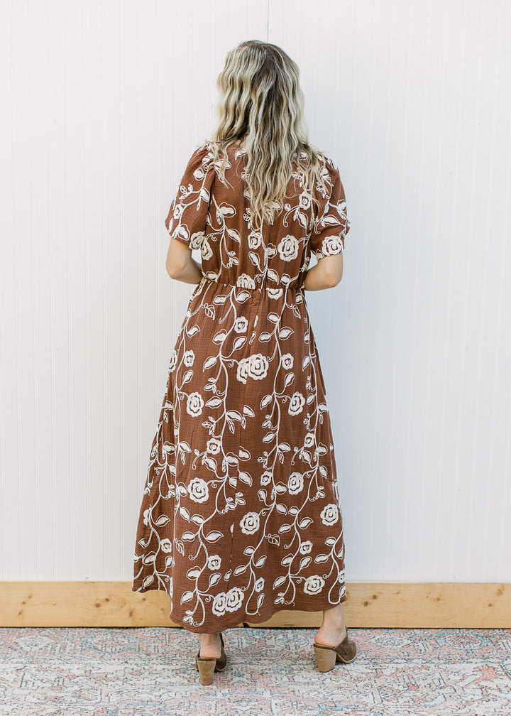 Back view of Model wearing a brown midi with embroidered cream floral, v-neck and short sleeves.