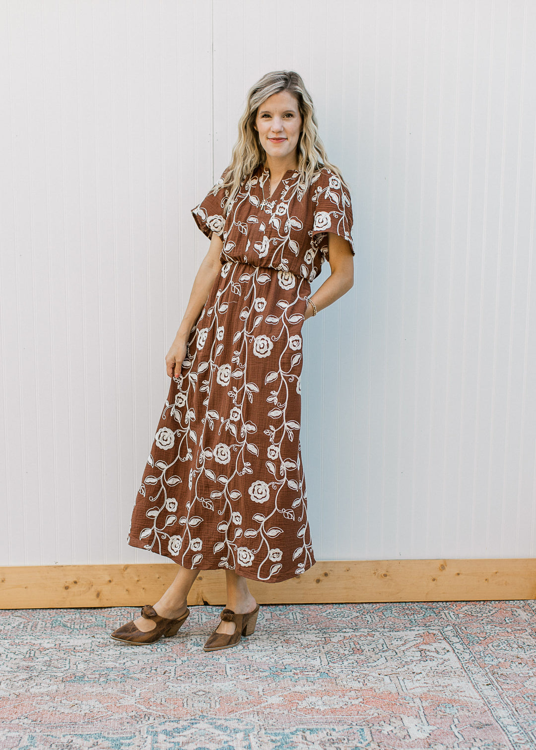 Model wearing heels and a brown midi with embroidered cream floral, v-neck and short sleeves.