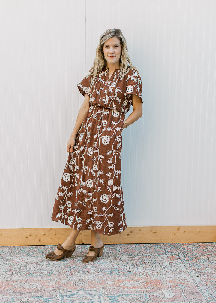 Model wearing heels and a brown midi with embroidered cream floral, v-neck and short sleeves.