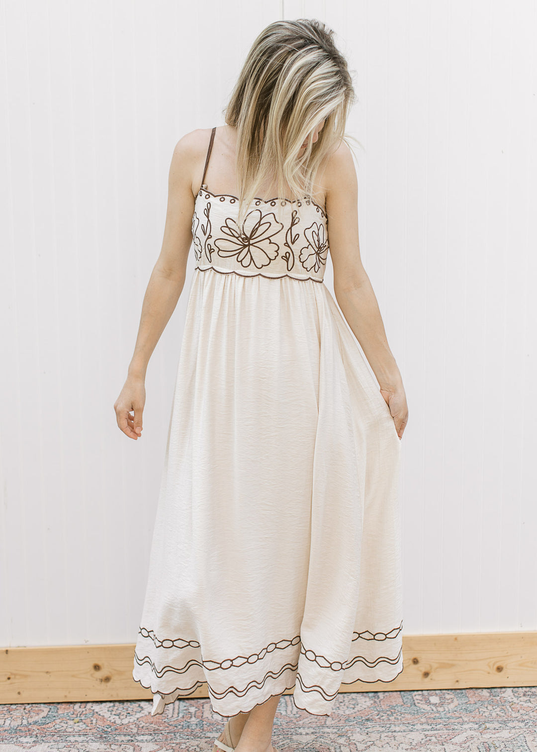 Model wearing a cream spaghetti strap midi with brown embroidered floral, scalloped neck and bust. 