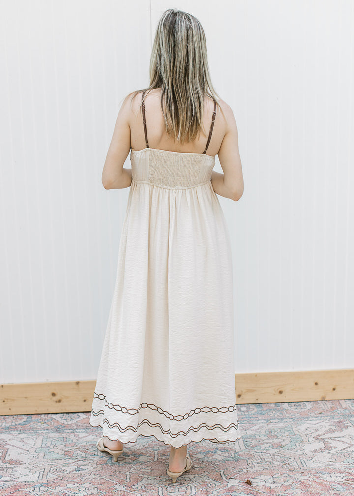 Back view of Model in a cream spaghetti strap midi with brown embroidery and smocked detail.