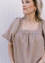 Model wearing a loose fit brown and white checkered top with a square neck and bubble short sleeves.