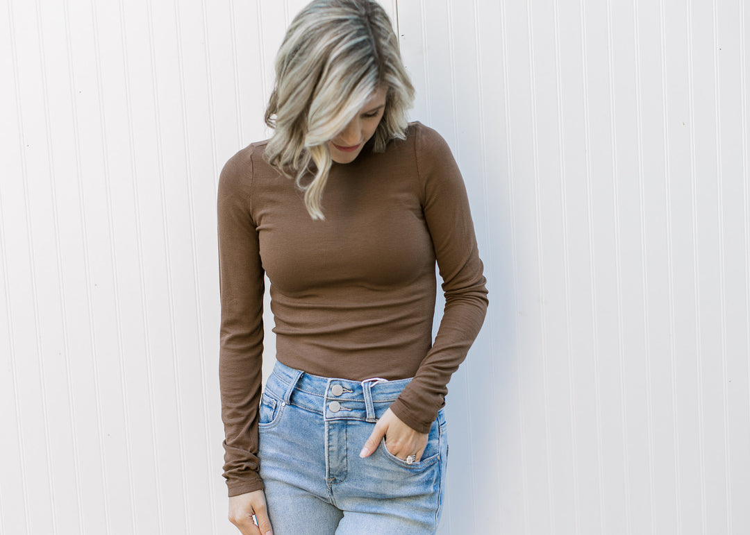 Model wearing jeans and a brown form fitted top with a ribbed material, mock neck and long sleeves.