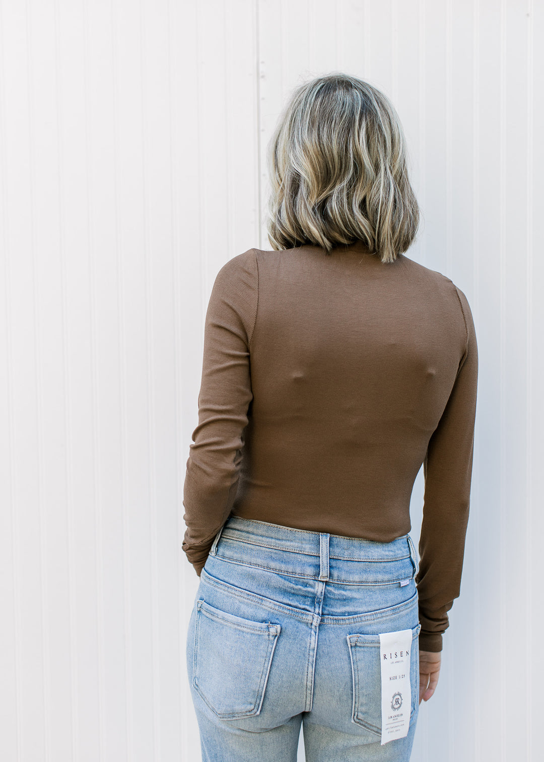 Back view of Model wearing a brown fitted ribbed top with a mock neckline and long sleeves.