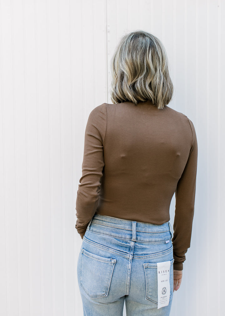 Back view of Model wearing a brown fitted ribbed top with a mock neckline and long sleeves.
