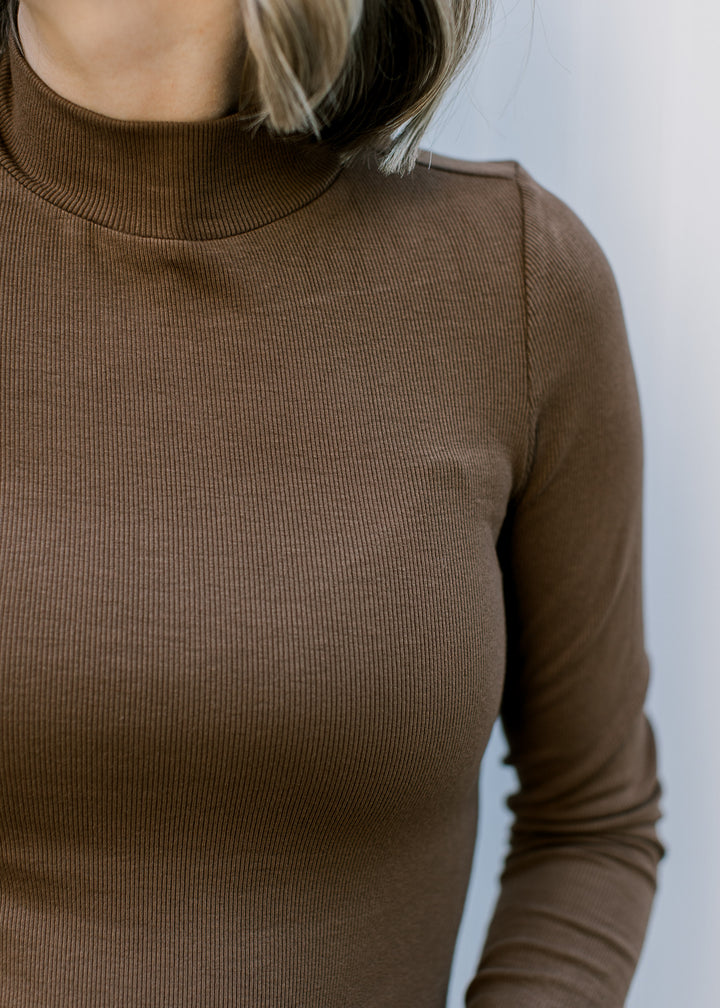 Close up of ribbed material and mock neckline on a brown form fitted, long sleeve top. 