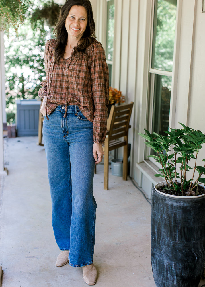Model wearing jeans, flats and a blush and brown gingham top with a smocked neck and flowy fit.