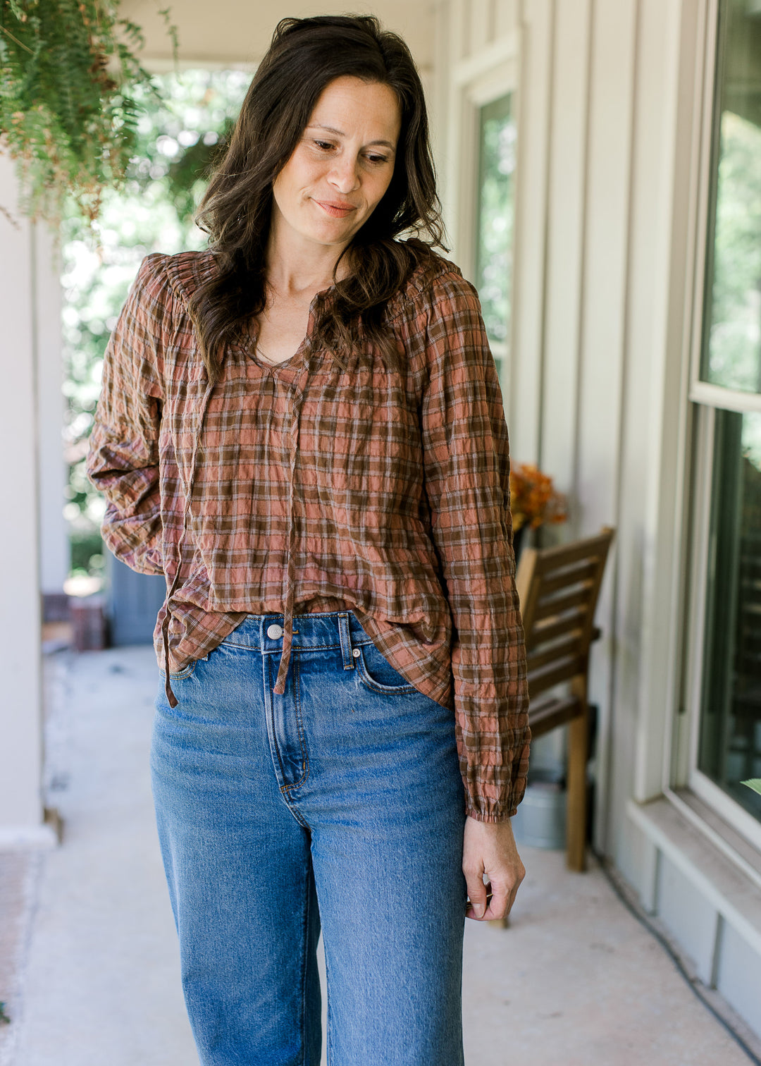 Model wearing a long sleeve blush and brown gingham top with a smocked neck and flowy fit.