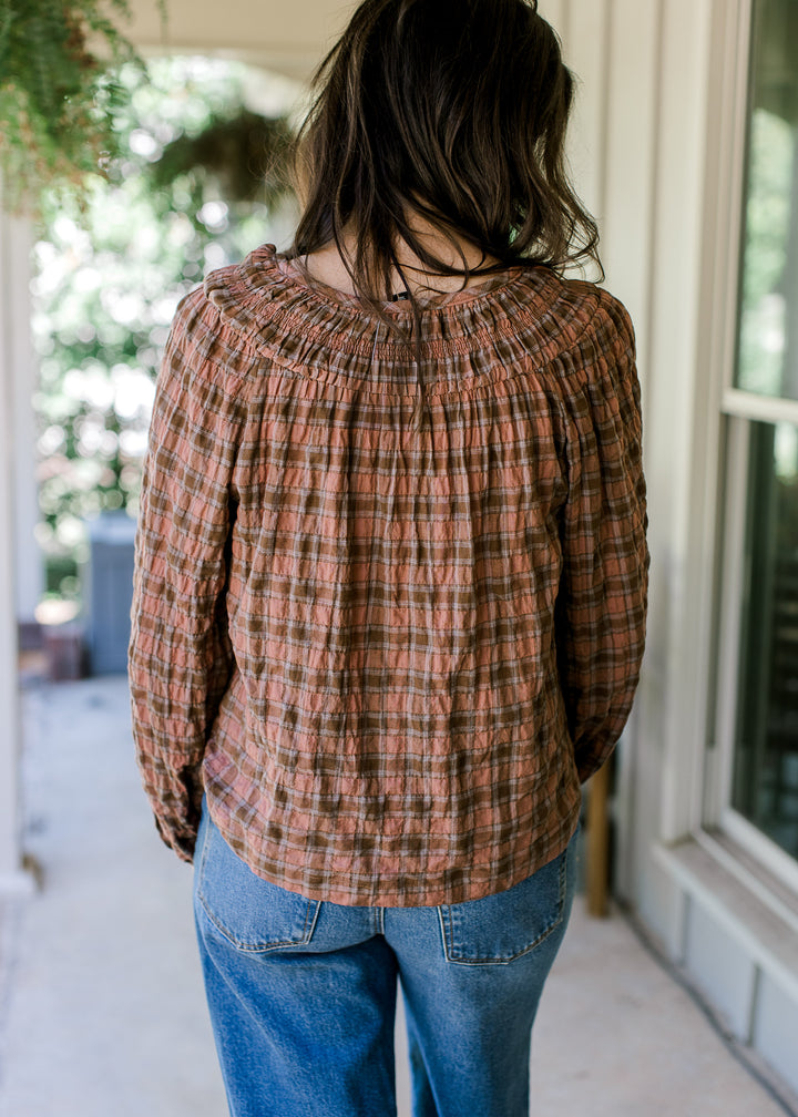 Back view of a long sleeve blush and brown gingham top with a smocked neck and flowy fit.