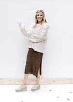 Model wearing a cream sweater with a brown knit midi with split sides and cream mules. 