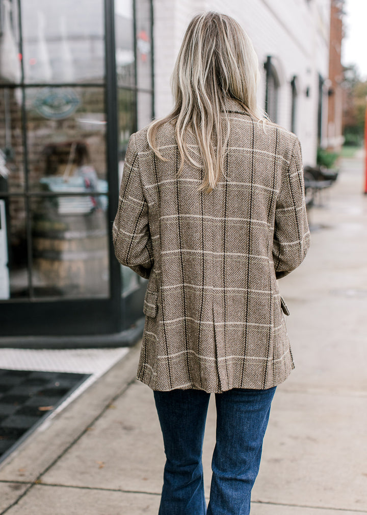 Back view of Model wearing a brown and cream plaid blazer with long sleeves and split seam back. 