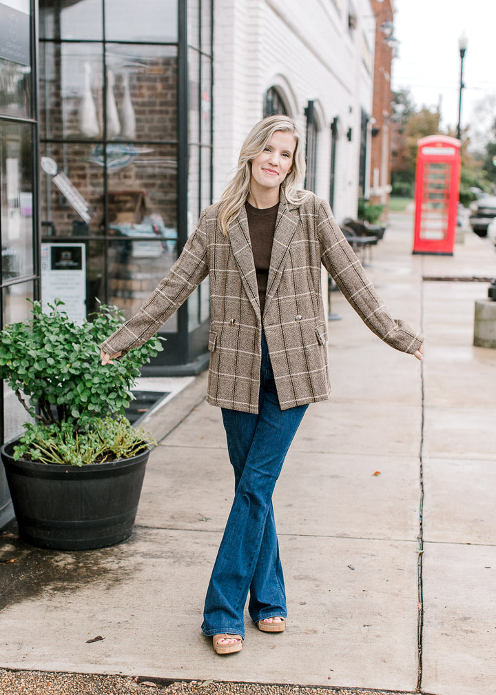 Model wearing a brown top and a brown and cream plaid blazer with double-breasted front.