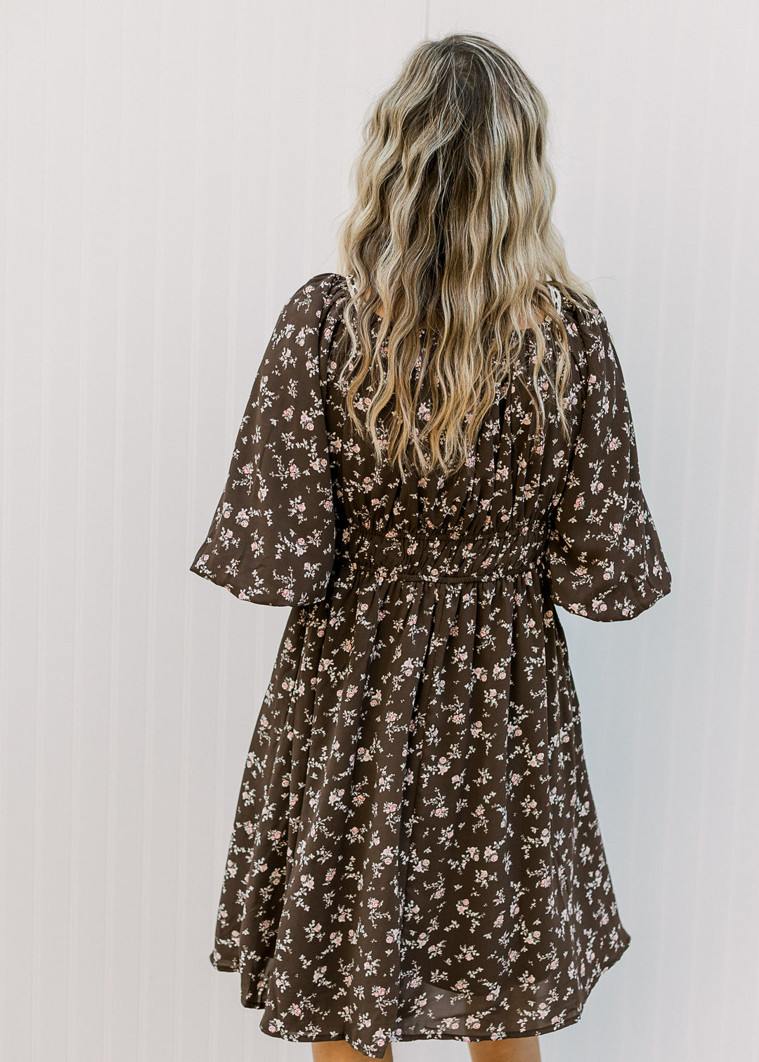 Back view of Model wearing a brown dress with elastic waist and 3/4 bubble sleeves. 