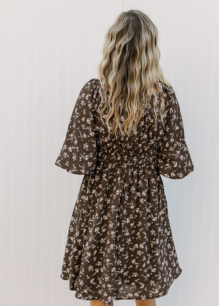 Back view of Model wearing a brown dress with elastic waist and 3/4 bubble sleeves. 